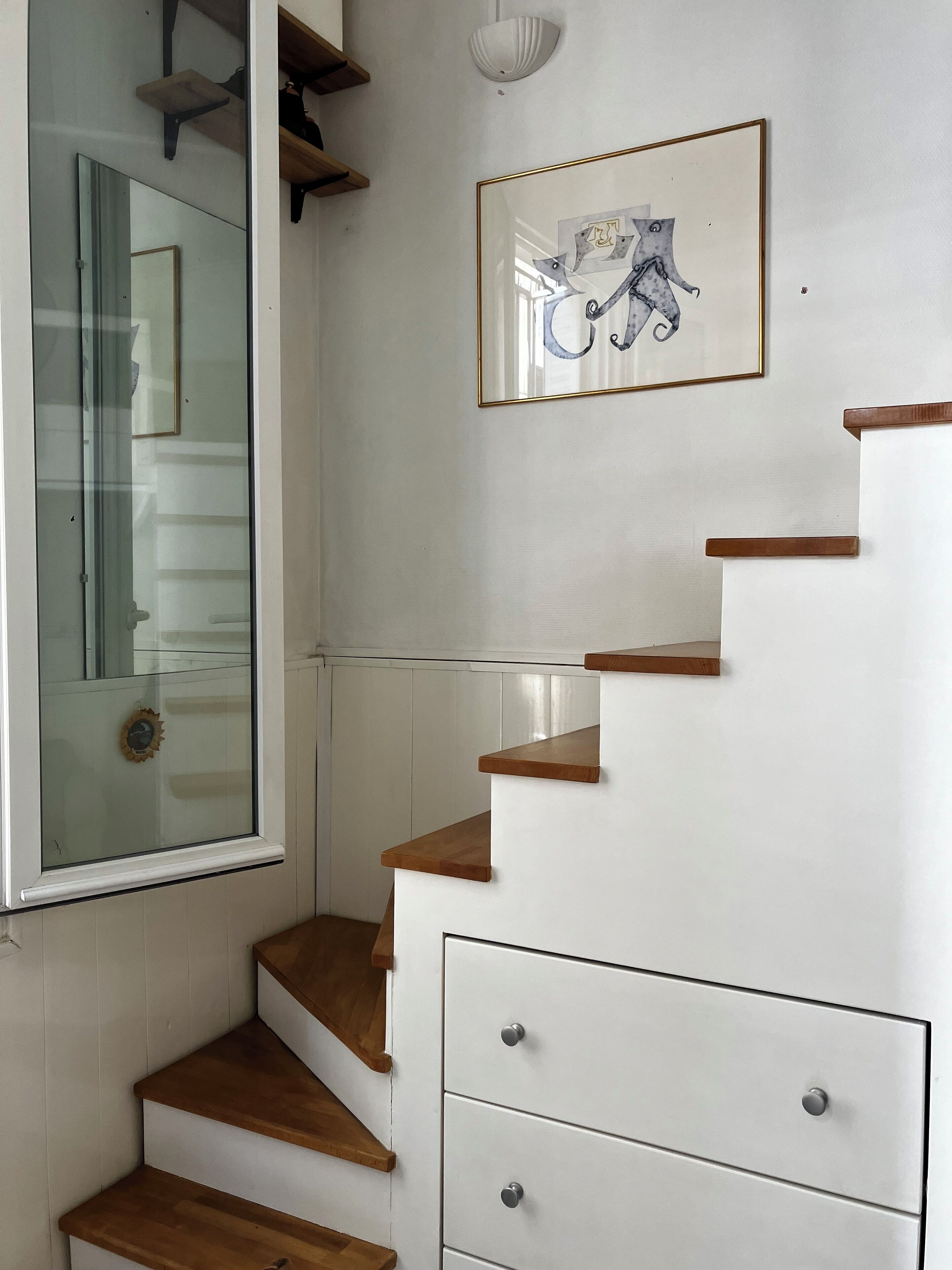 A staircase with wooden steps and white walls, a framed picture on the wall, and a clock on the wall.