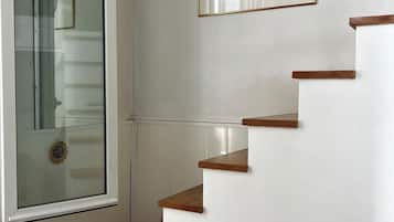 A staircase with wooden steps and white walls, a framed picture on the wall, and a clock on the wall.