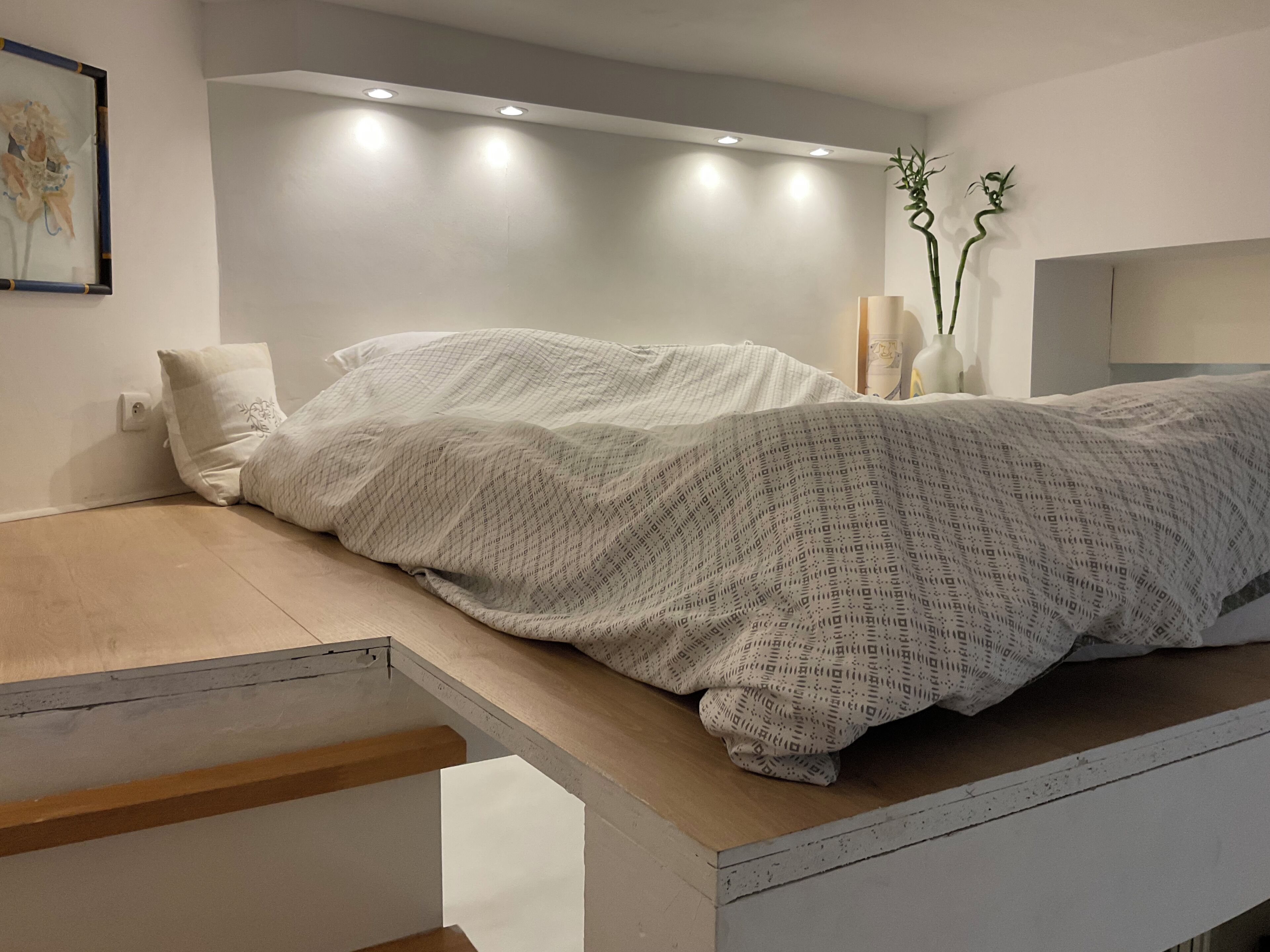 A modern bedroom with a bed, a nightstand, and a wall-mounted shelf.