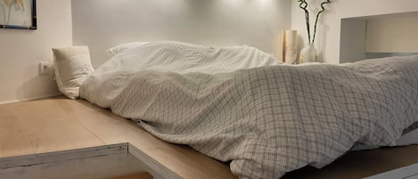 A modern bedroom with a bed, a nightstand, and a wall-mounted shelf.