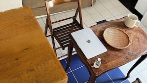 A room with a brown sofa, wooden chairs, a wooden table with a laptop, a woven basket, and a white mug. - Charming apartment Paris center république (Paris)