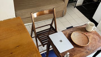 A room with a brown sofa, wooden chairs, a wooden table with a laptop, a woven basket, and a white mug.