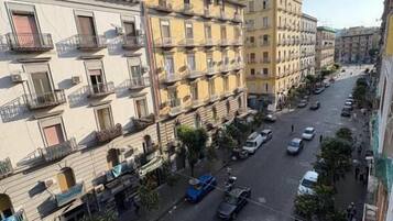 A multi-story residential building with balconies, a street with parked cars, and a clear sky.