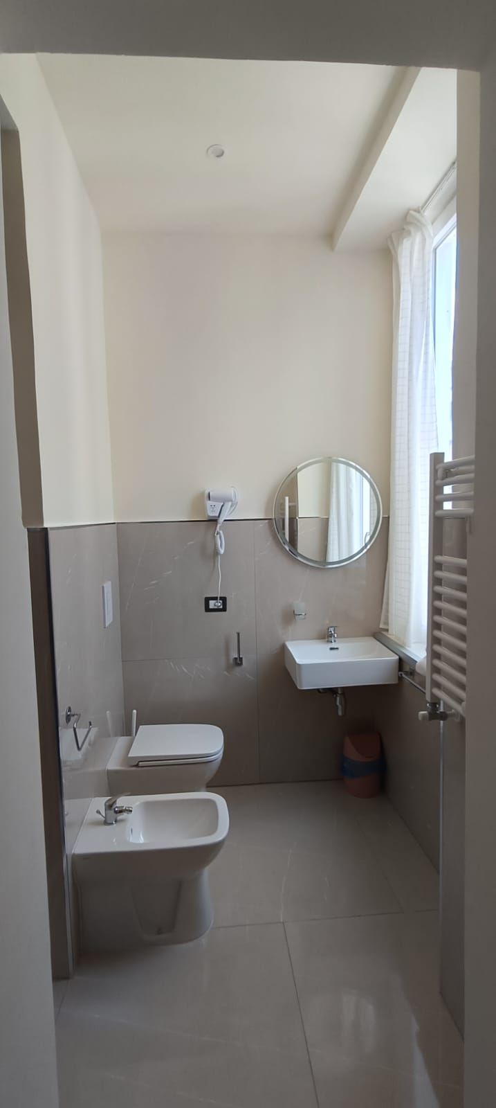 A small, modern bathroom with a toilet, bidet, sink, and mirror.