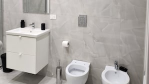 A modern bathroom with a white vanity, a large mirror, two bidets, and a toilet.