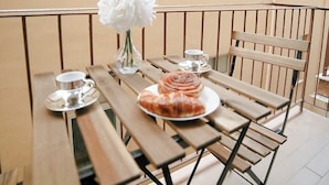 A wooden table with a plate of food and a white flower on a balcony with metal railings.