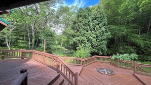 A wooden deck with a hot tub, surrounded by lush greenery and trees.