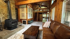 A cozy cabin interior with a stone fireplace, wooden beams, a brown leather sofa, and a wooden coffee table.
