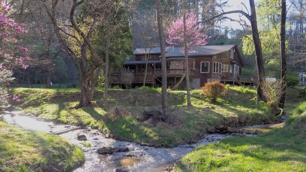 A rustic cabin with a wooden deck and a stream running through the property.