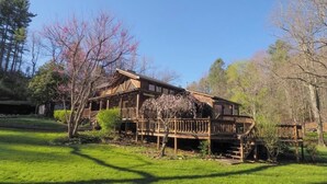 A wooden cabin with a deck, surrounded by trees and grass.