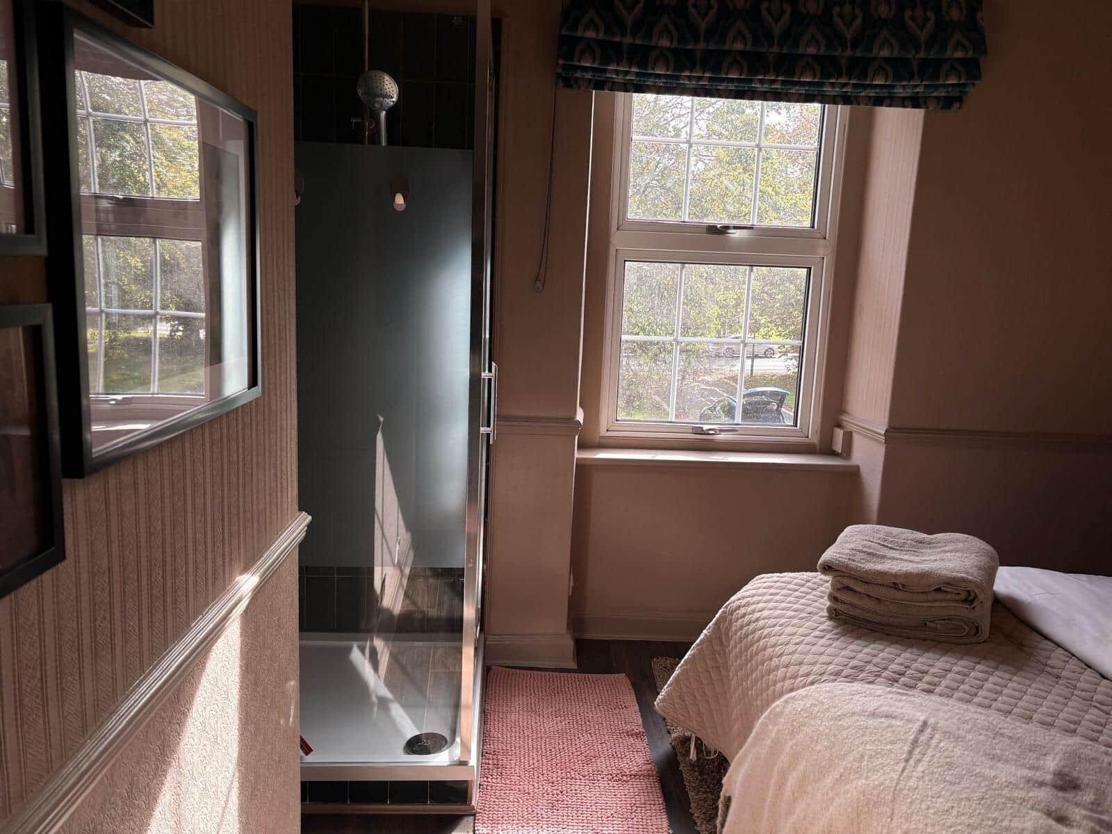 Ein Zimmer mit Dusche, einem Bett mit gesteppter Decke und einem Fenster mit blickdichtem Vorhang.