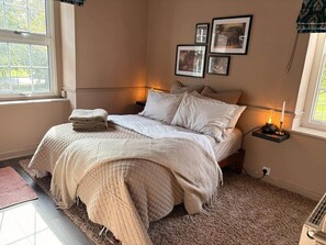 Un dormitorio con una cama, una mesita de noche con lámpara, una ventana y cuadros en la pared.
