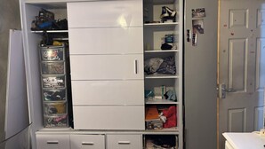 A compact, white storage unit with multiple drawers and shelves, containing various items like boxes, bags, and personal belongings. - Cosy room for Female Couple and Families (Manchester)
