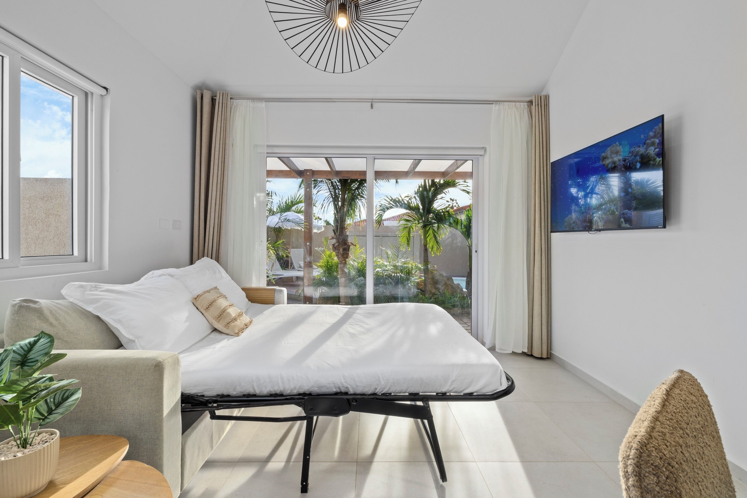A modern bedroom with a bed, a sofa, a TV, and a balcony with plants.