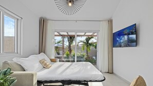 Ein modernes Schlafzimmer mit Bett, einer Couch, einem Fernseher und einem Balkon mit Pflanzen.