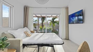 A modern bedroom with a bed, a sofa, a TV, and a balcony with plants.