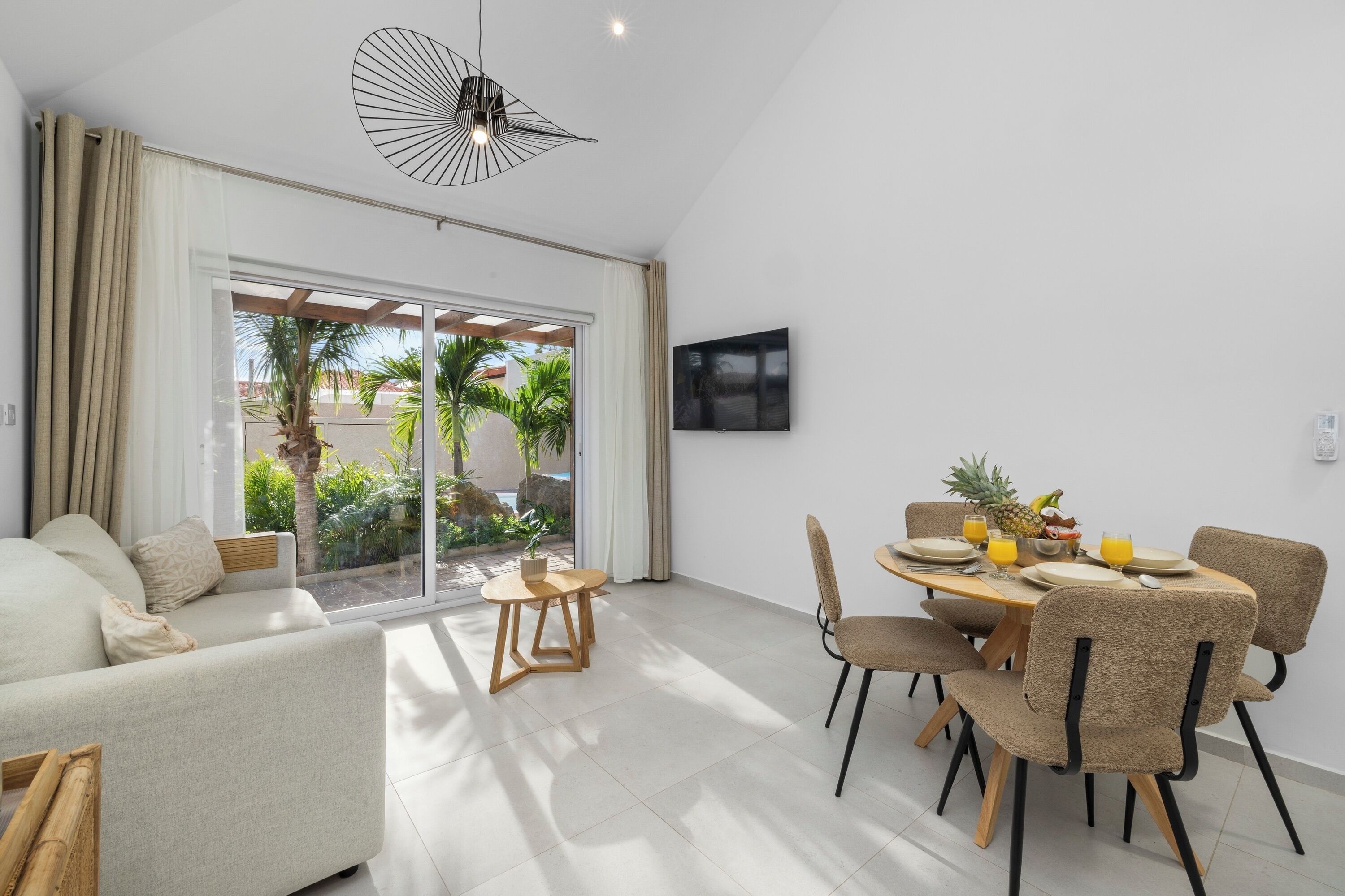 A modern living room with a sofa, dining table, chairs, and a TV mounted on the wall.