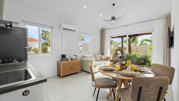 A modern kitchen with a built-in stove, a dining area with a round table and chairs, and a large window offering a view of palm trees and a house.