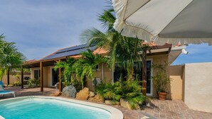 Ein Swimmingpool mit Liegestühlen, umgeben von Palmen und Topfpflanzen.
