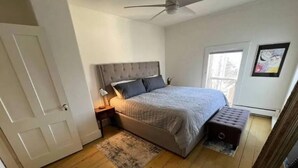 A bedroom with a bed, a nightstand, a floor lamp, a window, and a ceiling fan. - Damselfly Guesthouse (Newport)
