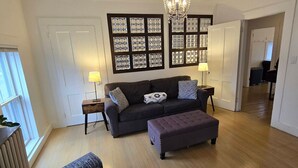 A living room with a dark sofa, a matching ottoman, a wall-mounted light fixture, and a framed map on the wall. - Damselfly Guesthouse (Newport)