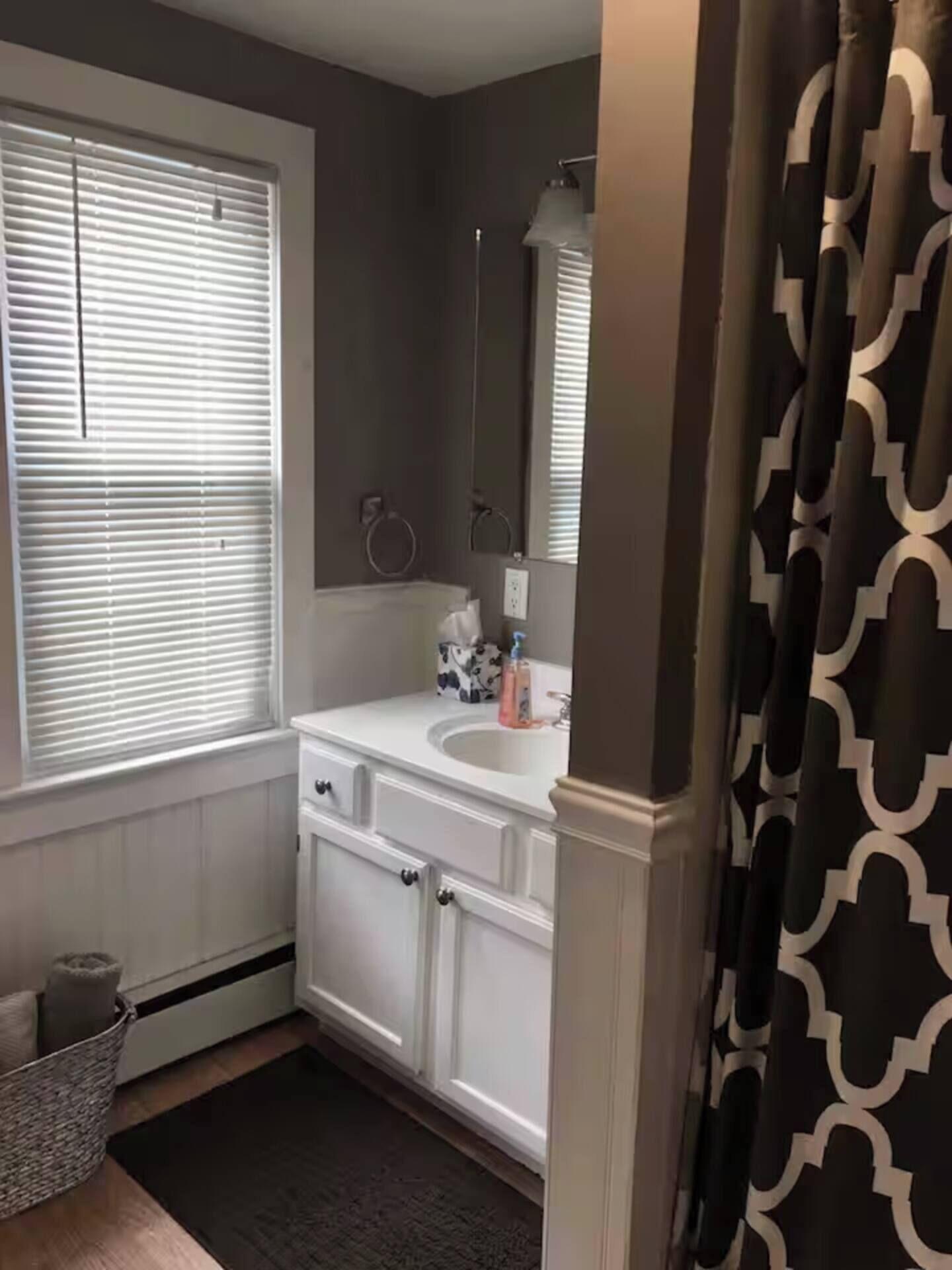 A bathroom with a white vanity, a mirror, and a window with blinds.