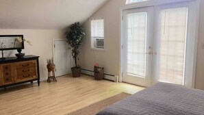 Een slaapkamer met een groot bed, een dressoir, een potplant en een raam met zonwering.