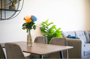 A dining table with a vase of flowers, a potted plant, and a sofa in the background. - Sea Esta in Cabo San Lucas (Cabo San Lucas)