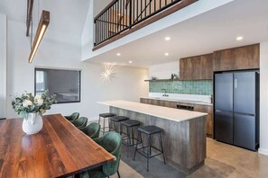 A modern kitchen with a central island, bar stools, a dining table, and a staircase.