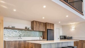 Een moderne keuken met een centraal eiland, barkrukken en een trap.