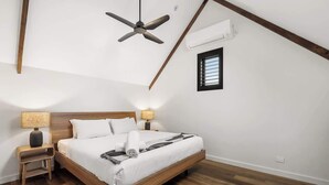 Een slaapkamer met een houten bed, een plafondventilator, een nachtkastje met een lamp en een raam met jaloezieën.