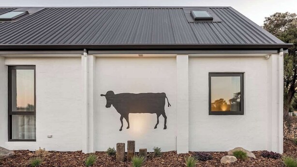 Een modern gebouw met een witte gevel, een silhouet van een koe en twee ramen.