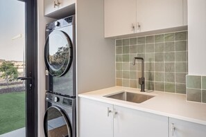 A laundry area with stacked washers and dryers, a sink, and a view of the outdoors.