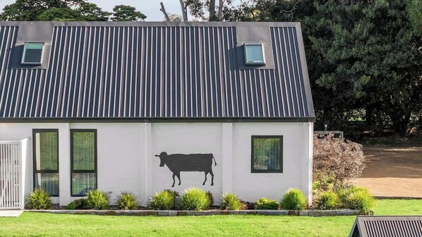A modern building with a metal roof, a cow mural, and a small window.