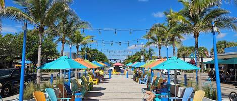 A beachside seating area with colorful umbrellas and chairs, palm trees, and a clear blue sky.