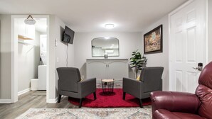A living room with two grey armchairs, a red rug, a red leather sofa, a TV, a mirror, and a painting on the wall. - Lovely cozy cottage with AC in charming Waycross (Waycross)