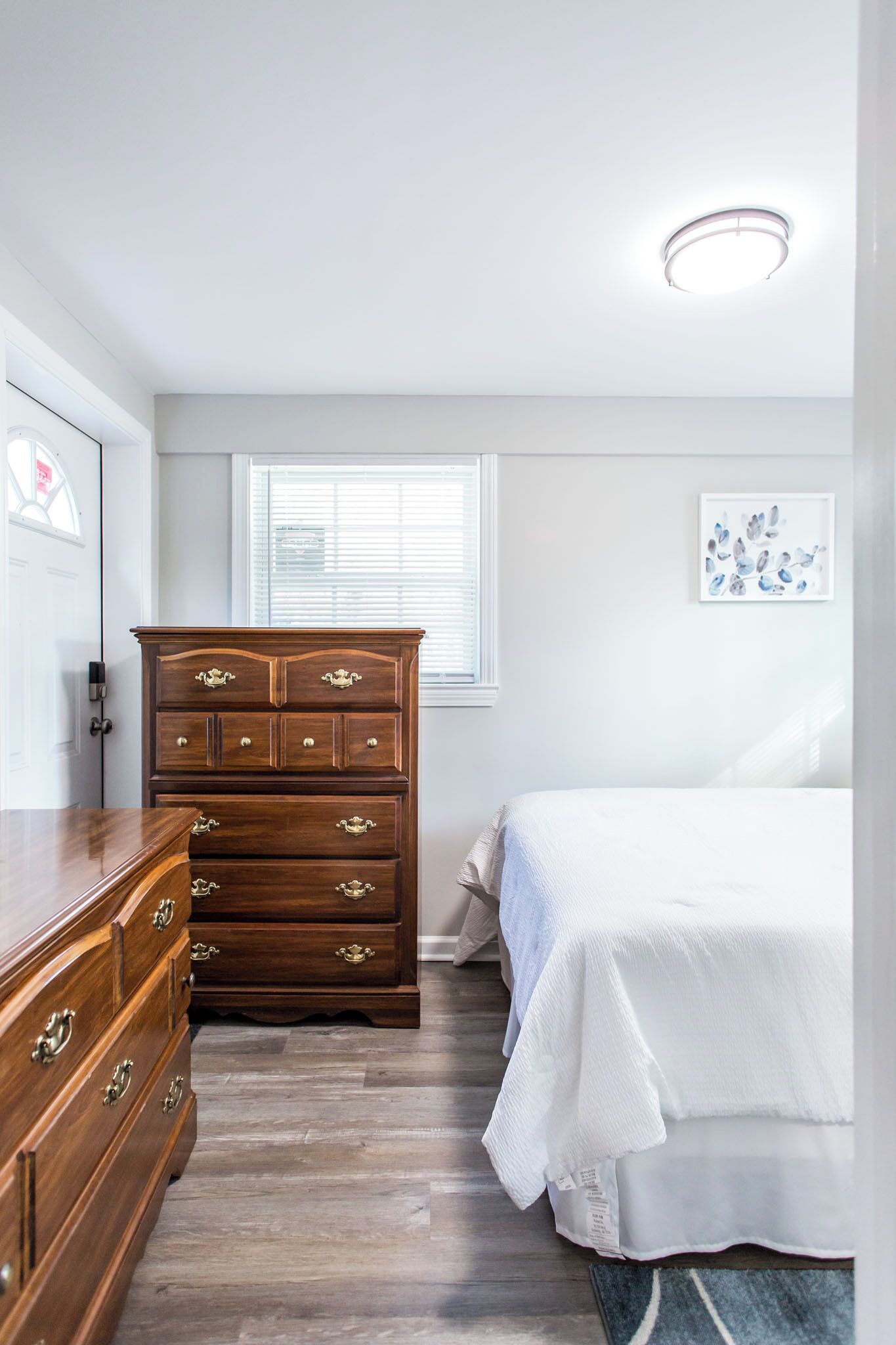 Un dormitorio con un aparador de madera, una cama, un ventanal con persianas y una lámpara en el techo.