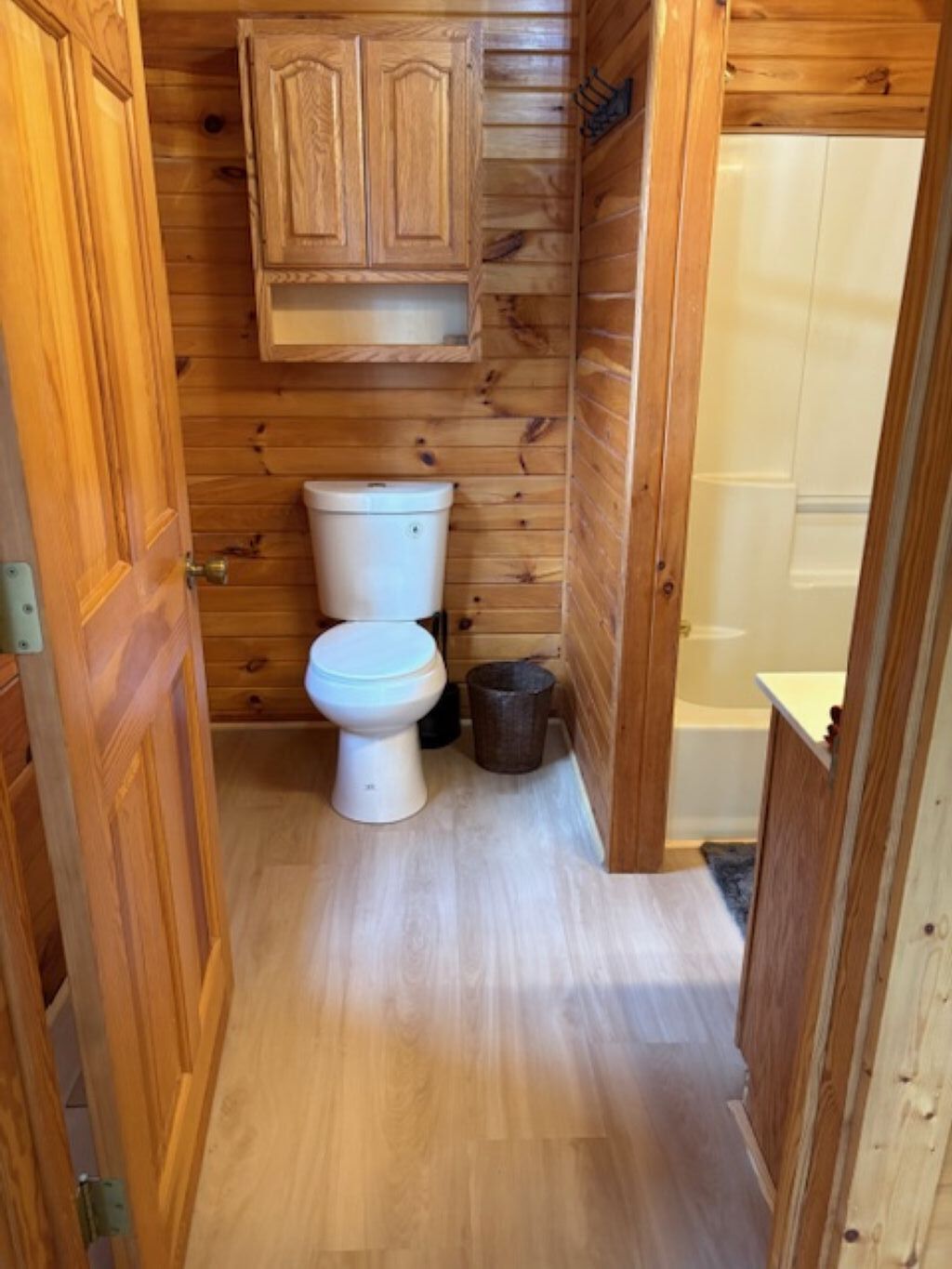 Ein kleines Badezimmer mit Holzverkleidung, ausgestattet mit Toilette, Mülleimer und Duschbereich.