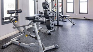 Una palestra con attrezzature per l'allenamento con i pesi, ampie finestre e un pavimento nero screziato.