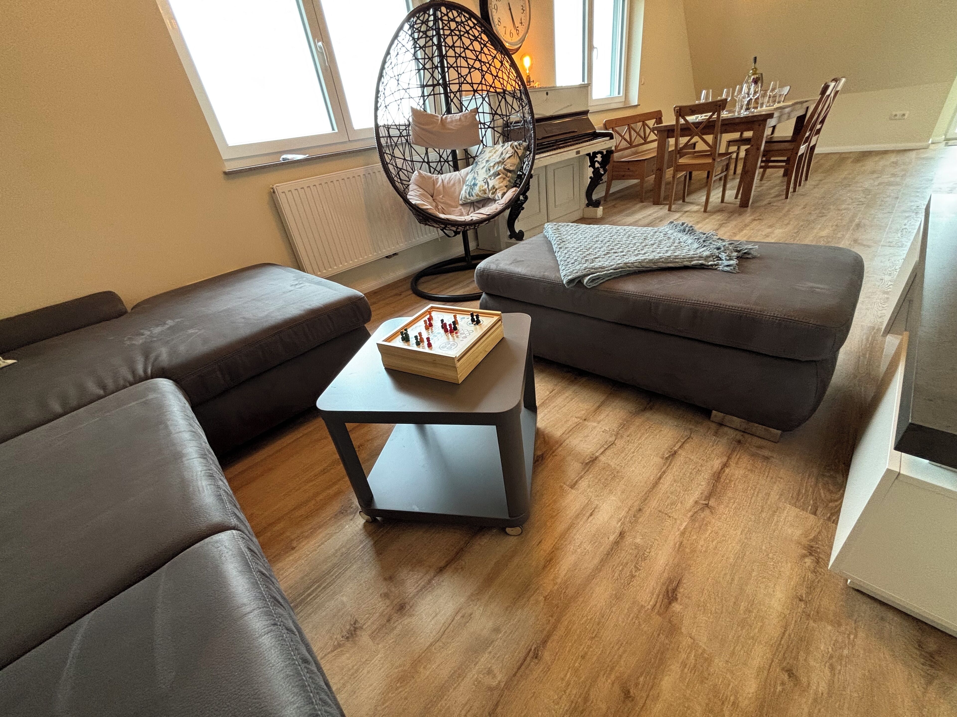 Ein modernes Wohnzimmer mit einer Couch, einem kleinen Tisch mit Schachspiel und einem Essbereich mit Stühlen und Tisch.