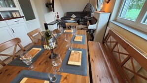 Een eetruimte met een houten tafel gedekt voor een maaltijd, een hangstoel en uitzicht op de omgeving door een raam.