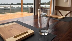 Een glas water op een houten tafel, met uitzicht op een groen veld door een raam.