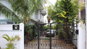 Una entrada porticada a un edificio residencial de fachada blanca, con un balcón y un cartel que indica la dirección.