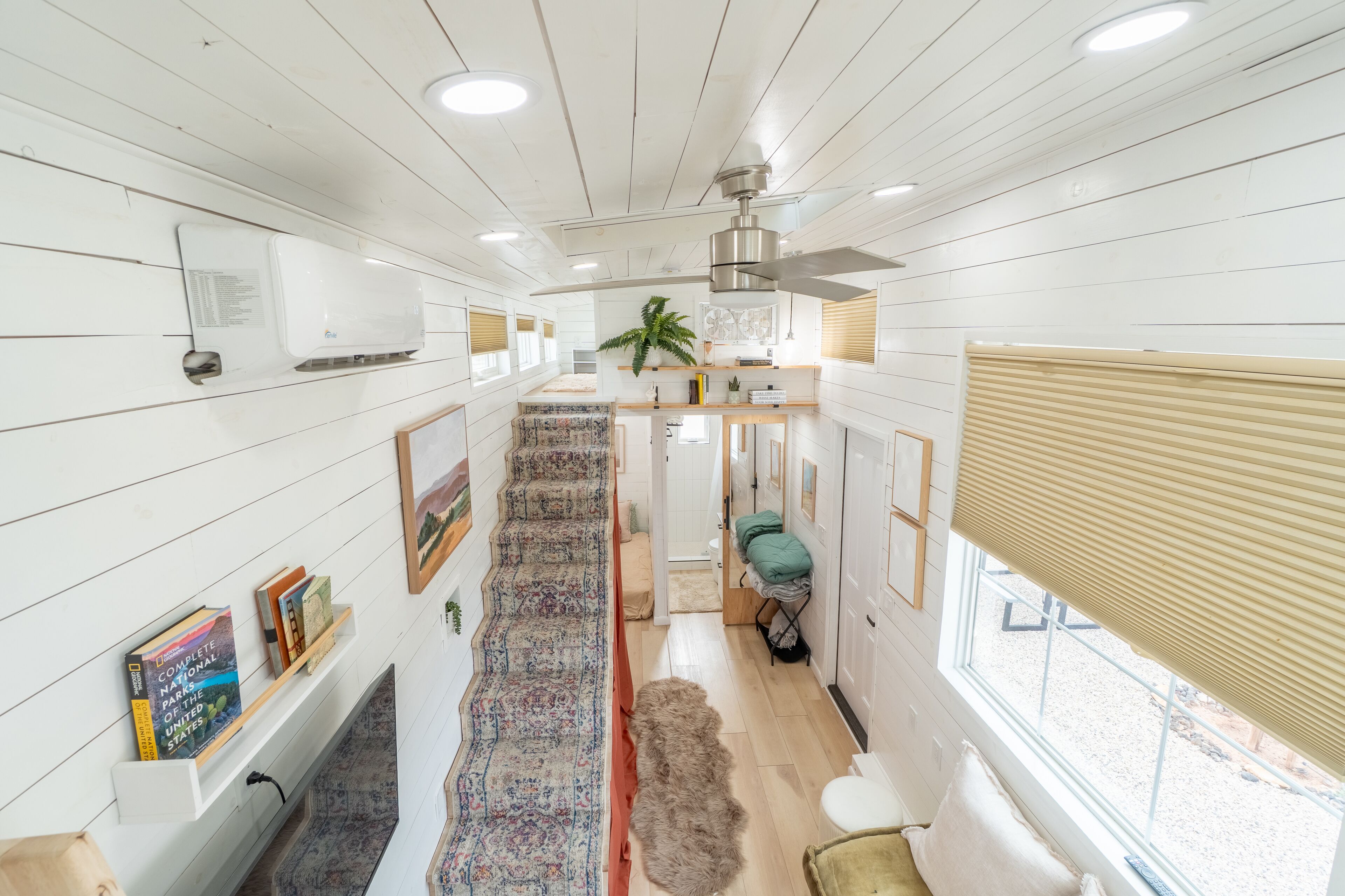 A spacious hallway with a patterned carpet, a ceiling fan, and a window with blinds.