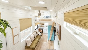 A narrow, multi-level interior with white wooden walls, a central staircase, and a kitchen area.