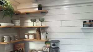 A modern kitchen with white cabinetry, wooden shelves, and a coffee maker.