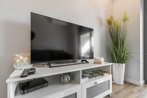 Ein Flachbildfernseher auf einer weißen Unterhaltungseinheit mit Fernbedienung, einem Laptop und einer dekorativen Kugel.