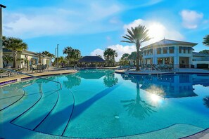 Une grande piscine extérieure à l’eau d’un bleu limpide, entourée de palmiers et bordée d’un bâtiment à toit de chaume.