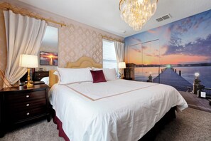 Une chambre d’hôtel avec un grand lit, une table de chevet, un miroir et une fresque murale représentant un coucher de soleil sur l’eau.