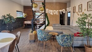 Ett modernt vardagsrum med en grå soffa, blå fåtöljer med blommönster, en trätrappa och en banderoll med texten ”BLIVANDE BRUD”.